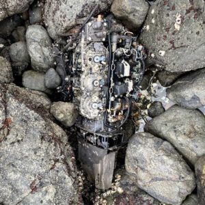 Boat motor sitting on top of grey rocks found on a beach cleanup but not recovered