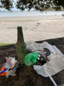 Trash collected on a beach walk featuring a green beer bottle, dog poop bag (sans poop), plastic wrapper, map, and plastic ziplock bag