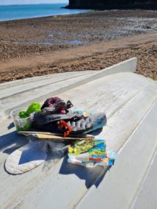 Trash collected on a beach walk featuring a flip flop, shoe insert, ramen noodle packet, fishing wire, and misc plastic items